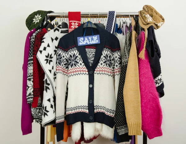 Cute winter sweaters displayed on hangers with a big sale sign.