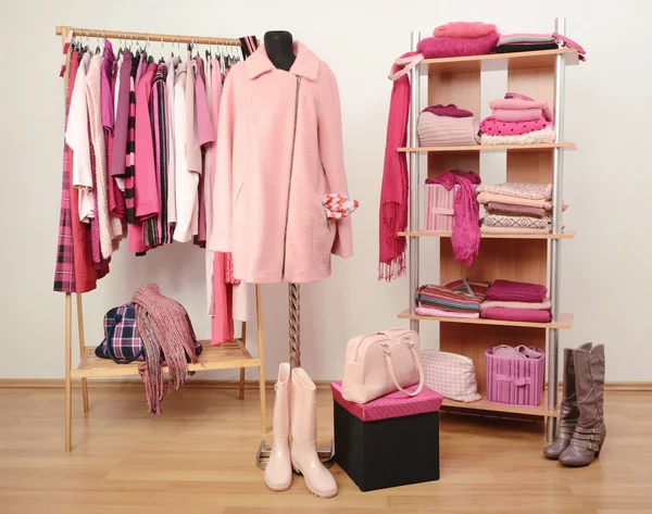 Dressing closet with pink clothes arranged on hangers and shelf, a coat on a mannequin.