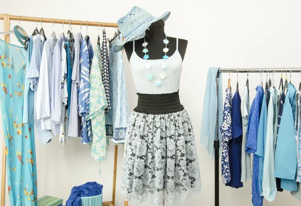 Dressing closet with blue clothes arranged on hangers and a summer outfit on a mannequin.