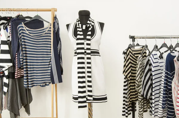 Dressing closet with striped clothes arranged on hangers and a black and white outfit on a mannequin.