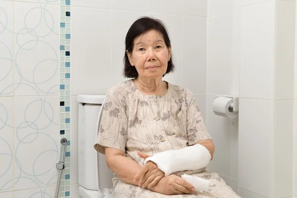 Senior women broken arm in cast using the toilet.
