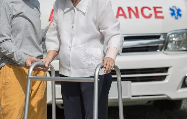 Senior woman using a walker with caregiver to take ambulance