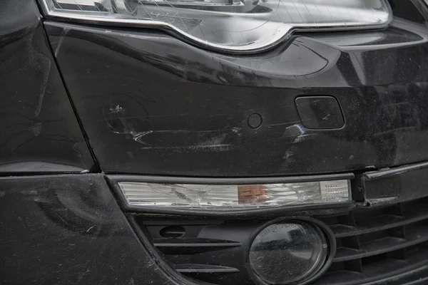 Close up on black bumper car scratched with deep damage to the paint.