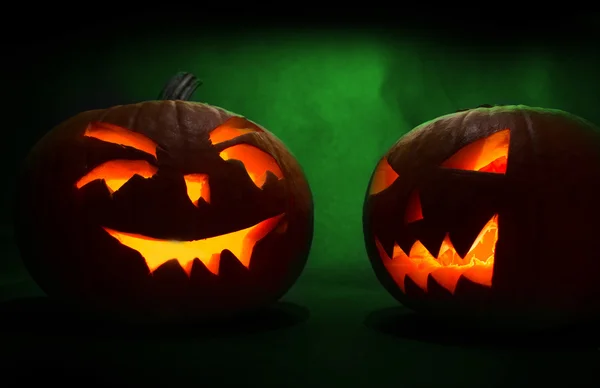 Two carved faces of pumpkins glowing on Halloween on green background