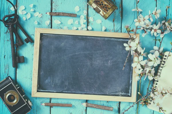 Top view image of spring white cherry blossoms tree, blackboard, old camera on blue wooden table