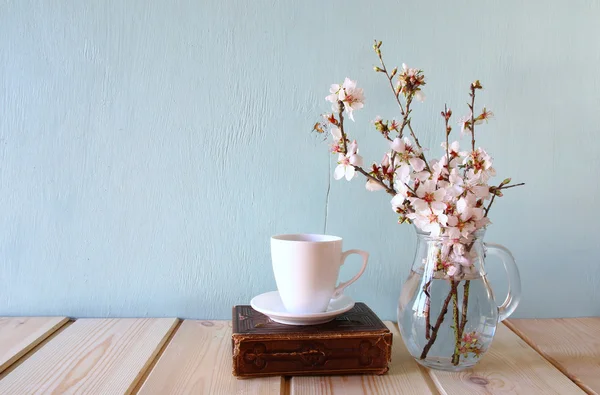 Old book, cup of coffee next to spring white flowers on wooden texture