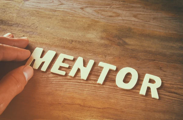 Male hand spelling the word mentor from wooden letters over wooden table background. retro style image