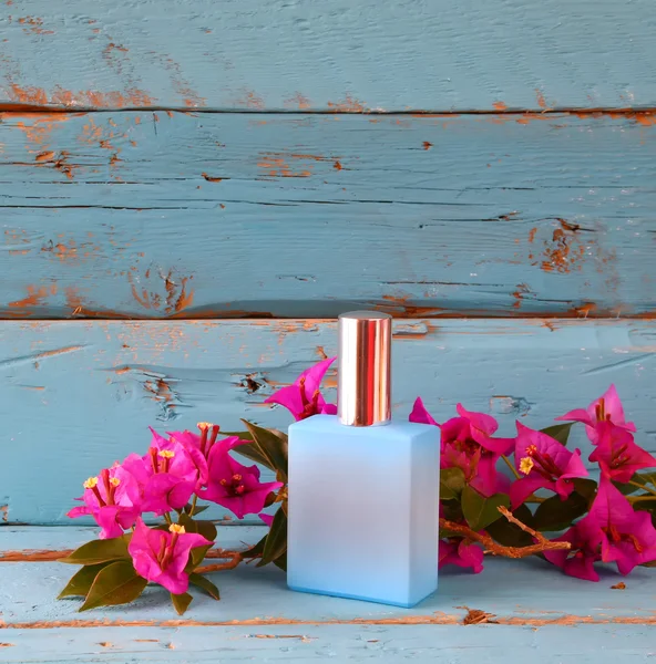 Vintage perfume bottle next to bougainvillea flowers on wooden table