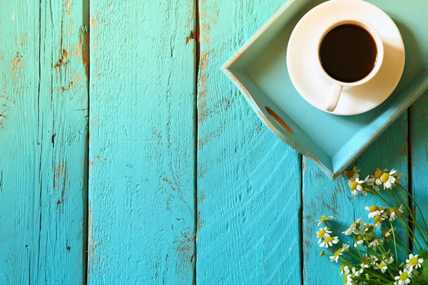 Top view image of daisy flowers next to cup of coffee on blue wooden table. vintage filtered