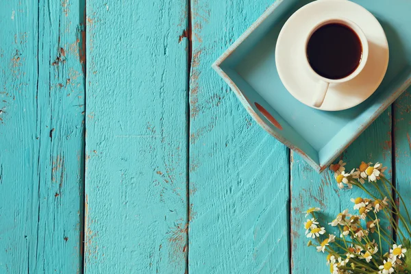 Top view image of daisy flowers next to cup of coffee on blue wooden table. vintage filtered