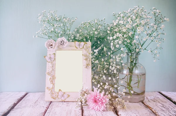 Vintage filtered and toned image of pink and white flowers and antique frame on wooden table. template, ready to put photography