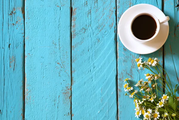 Top view image of daisy flowers next to cup of coffee on blue wooden table. vintage filtered and toned