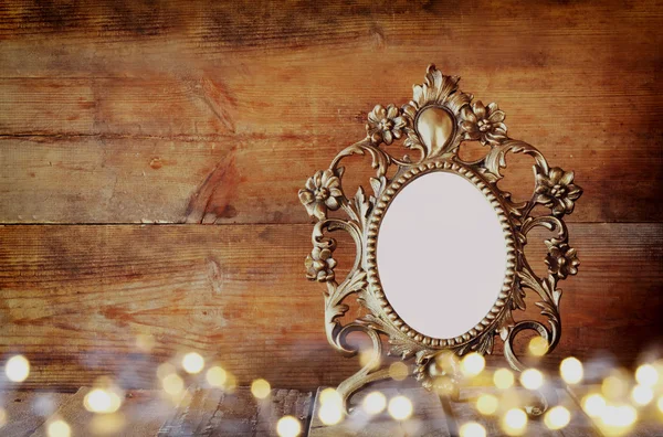 Double exposure image of Antique blank victorian style frame and gold lights on wooden table. vintage filtered image. template, ready to put photography