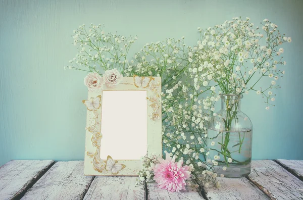 Vintage filtered and toned image of image of pink and white flowers and antique frame on wooden table. template, ready to put photography