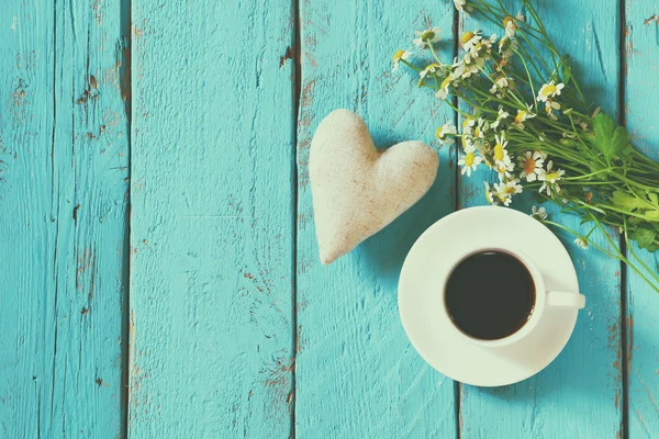 Top view image of daisy flowers and fabric heart next to cup of coffee on blue wooden table. vintage filtered and toned