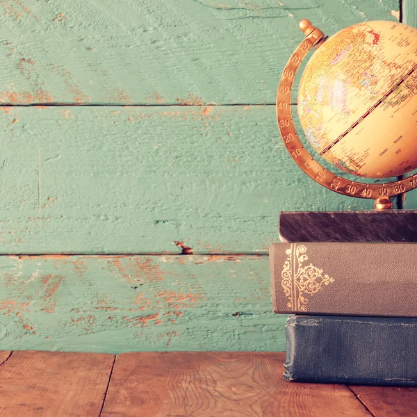 Top view photo of vintage globe and stack of books on wooden desk. vintage filtered image