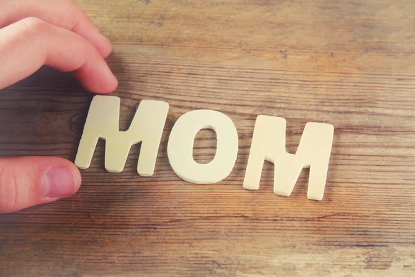 Word MOM made with block wooden letters on wooden background. vintage filtered and toned