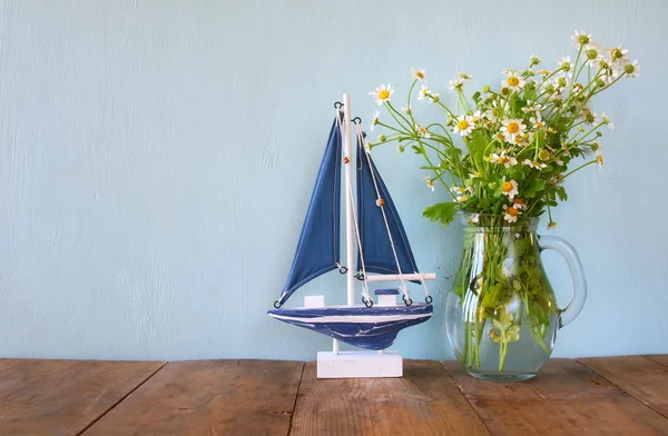 Fresh daisy flowers next to wooden boat on wooden table
