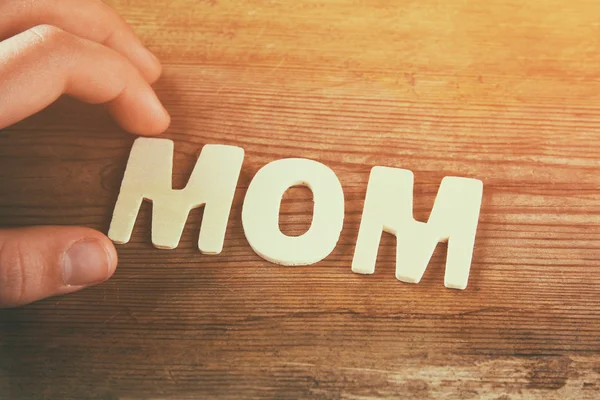 Word MOM made with block wooden letters on wooden background. vintage filtered and toned