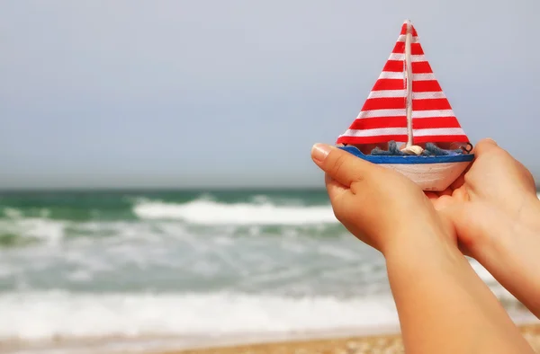 Woman\'s hands holding a boat in front of sea horizon