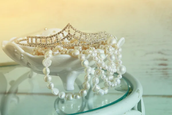 Image of white pearls necklace and diamond tiara on vintage table. vintage filtered. selective focus