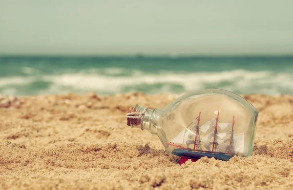 Boat in the bottle on sea sand and ocean horizon