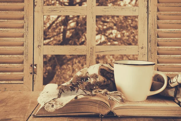 Romantic scene of cup of coffee next to old book in front of countryside view outside of the old rustic window. vintage filtered image