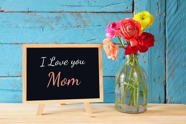 Flowers next to blackboard, on wooden table. happy mother's day concept