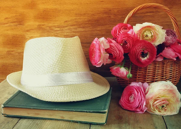 Fedora hat next to old book and flowers on wooden table