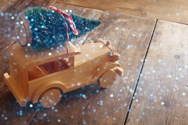 Wooden car carrying a christmas tree. Glitter overlay