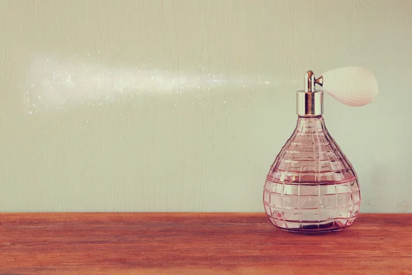 Vintage antigue perfume bottle with effect of perfume spray, on wooden table. retro filtered image