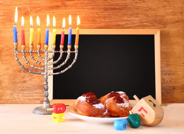 Jewish holiday Hanukkah with menorah, doughnuts over wooden table