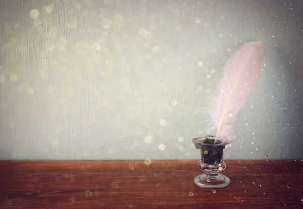 Low key image of white Feather, inkwell,  and glitter lights background on old wooden table