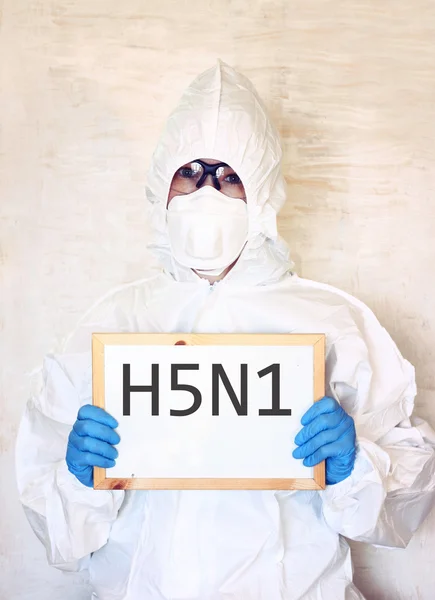 Lab scientist in safety suit holding board with word H5N1