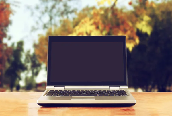 Laptop over wooden table outdoors and blurred background of trees in the forest