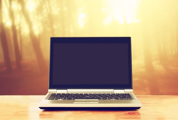 Laptop over wooden table outdoors and blurred background of trees in the forest