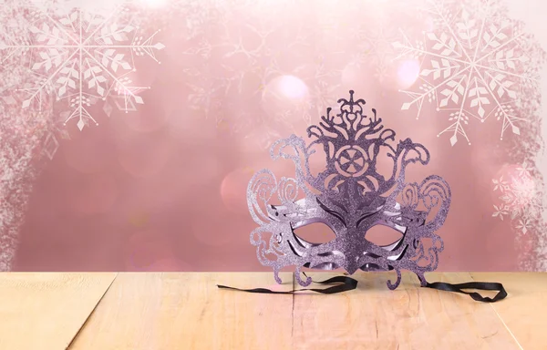 Mysterious Venetian masquerade mask on wooden table and glitter background with snowflake overlays