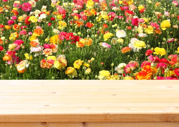 Wood board table in front of summer landscape of field with many flowers