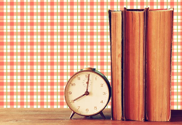 Stack of old books and old clock over wooden table and vintage style wallpaper