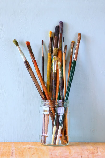 Paint brushes in jar over wooden aqua blue background