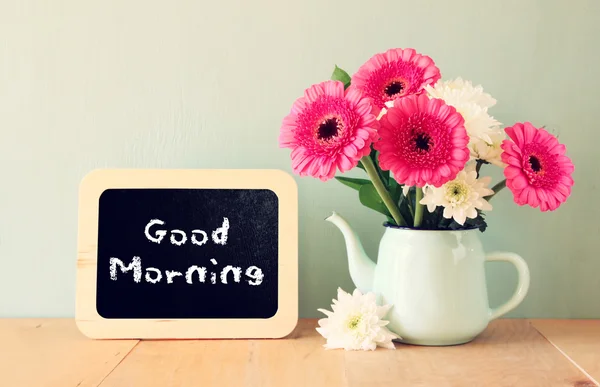 Blackboard with the phrase good morning written on it next to vase with fresh flowers
