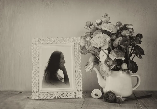 Summer bouquet of flowers and victorian frame with vintage portrait of young woman on the wooden table. black and white style image with textured overlay