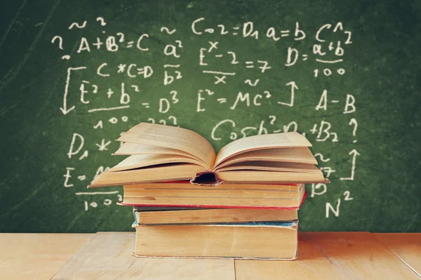 Image of school books on wooden desk over green background with formulas. education concept