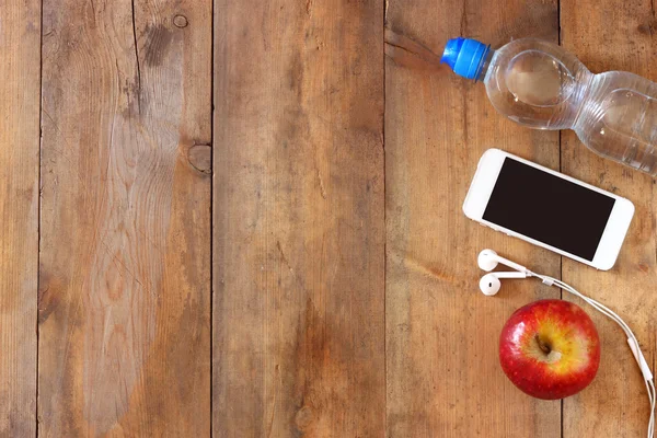 Fitness concept with bottle of water, mobile phone with earphones and apple over wooden background. filtered image