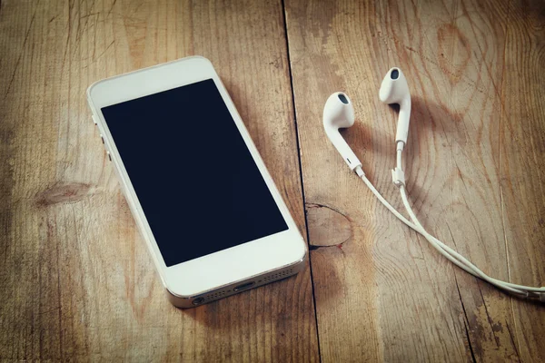 Top view of white smart phone and earphones on wooden table