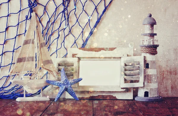 Old vintage wooden white frame, lighthouse, starfish and sailing boat on wooden table. vintage filtered image. nautical lifestyle concept. with glitter overlay