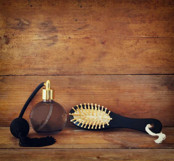 Photo of vintage perfume bottle next to old wooden hairbrush on wooden table. retro filtered image