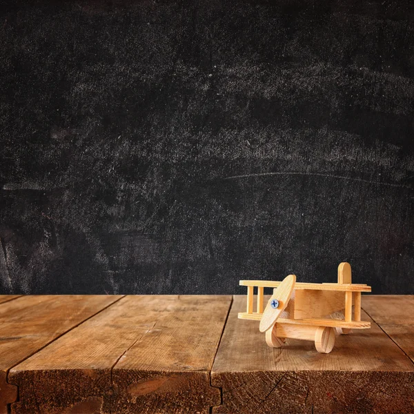 Image of wooden toy airplane over wooden table against chalk blackboard
