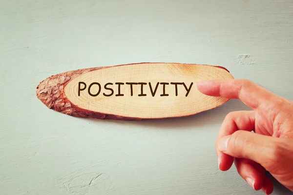 Image of male hand pointing at wooden sign with the word positivity.