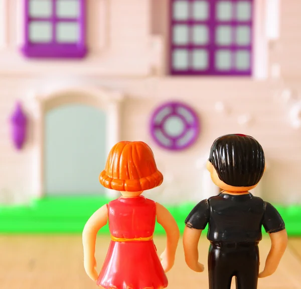 Concept image of young couple in front of new house. little plastic toy dolls (male and female) , selective focus